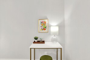 A white table with a framed artwork, a lamp, and a small plant on a white wall. - Pool + Free Parking | 2BR Galveston Hideout (Galveston)