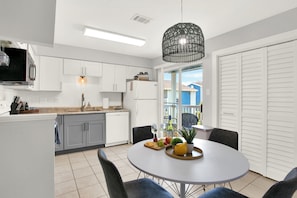 A modern kitchen with white cabinets, a dining area with a round table, and a view of the outside. - Pool + Free Parking | 2BR Galveston Hideout (Galveston)