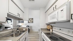 A modern kitchen with granite countertops, stainless steel appliances, and white cabinetry. - Palms Escape | Ocean View Condo | Pool | Pet-Friendly Retreat (Galveston)