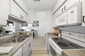 A modern kitchen with granite countertops, stainless steel appliances, and white cabinetry. - Palms Escape | Ocean View Condo | Pool | Pet-Friendly Retreat (Galveston)