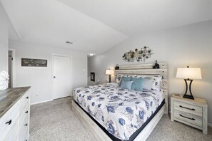 A bedroom with a bed, bedside tables, a dresser, and a wall-mounted artwork. - Palms Escape | Ocean View Condo | Pool | Pet-Friendly Retreat (Galveston)