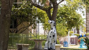 A Dalmatian statue in a park with a bench, a tree, and a fence in the background. - Palms Escape | Ocean View Condo | Pool | Pet-Friendly Retreat (Galveston)