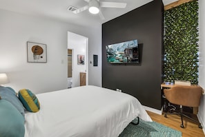 A modern bedroom with a bed, a desk, and a chair. There is a painting on the wall and a plant on the right side. - 2 Workspaces + Pool | Couples’ Galveston Escape (Galveston)