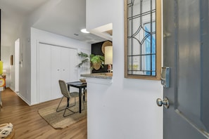 A modern kitchen with white cabinetry, a dining area with a table and chairs, and a large window with a view. - 2 Workspaces + Pool | Couples’ Galveston Escape (Galveston)