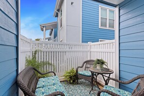 A patio with wicker furniture and a small table, surrounded by a white fence. - The Salty Siren | Mermaid-Themed Condo | Pool Access | Private Patio (Galveston)