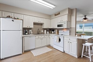 A modern kitchen with white cabinetry, a built-in microwave, and a refrigerator. - The Salty Siren | Mermaid-Themed Condo | Pool Access | Private Patio (Galveston)