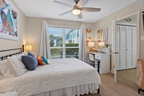 A bedroom with a bed, a desk, a chair, a ceiling fan, a window with curtains, and a door. - The Salty Siren | Mermaid-Themed Condo | Pool Access | Private Patio (Galveston)