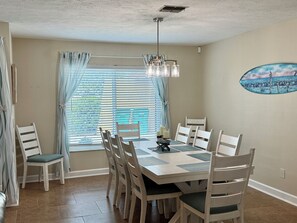 A dining area with a table set for six, surrounded by six chairs, a ceiling fan, and a window with blinds. - Deep Water Canal with 20' Floating Dock and Game Room (Crystal River)