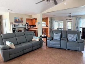 A living room with a sofa and a loveseat, a kitchen in the background, and a dining area. - Deep Water Canal with 20' Floating Dock and Game Room (Crystal River)