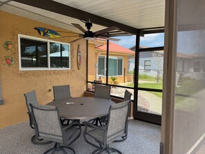 A covered patio with a table and chairs, a ceiling fan, and a view of a house with a red roof. - Deep Water Canal with 20' Floating Dock and Game Room (Crystal River)