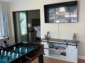 Ein Zimmer mit einem Kicker, einem an der Wand montierten Fernseher und einer Schiebetür zu einem weiteren Raum.