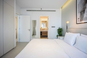 Ein modernes Hotelzimmer mit einem großen Bett, einem Nachttisch, einem Spiegel und einer Tür zu einem Badezimmer.
