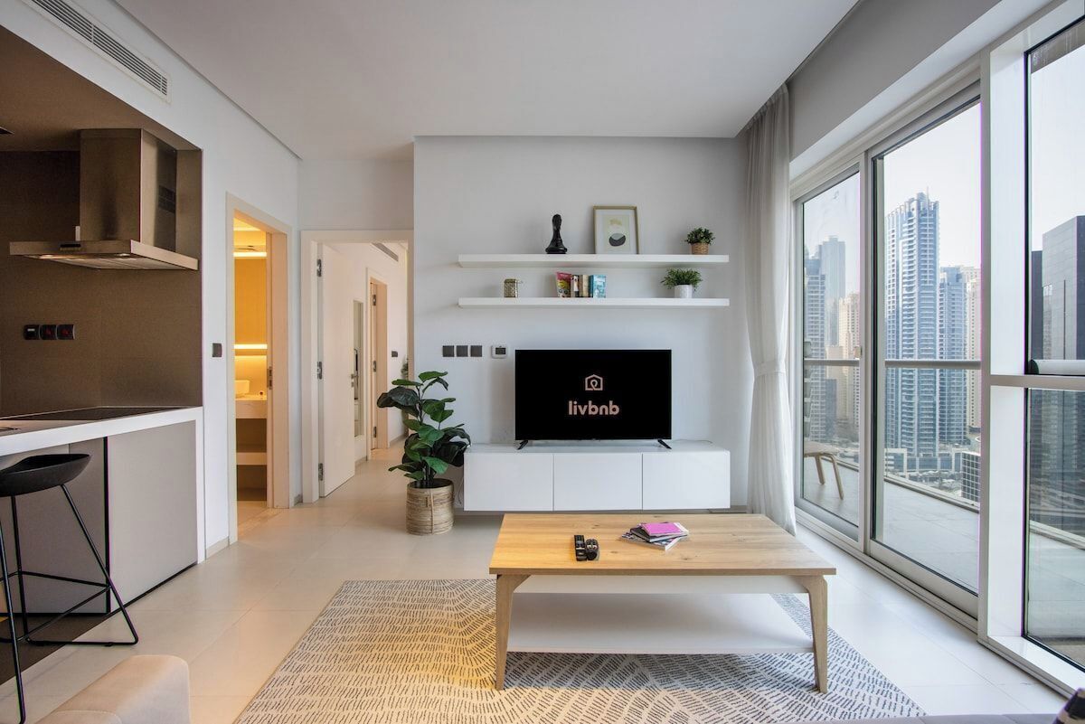 Ein modernes Wohnzimmer mit Flachbildfernseher, Couchtisch aus Holz und einem großen Fenster mit Blick auf die Stadt.