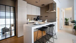 A modern kitchen with a central island, bar stools, and a view through a glass door. - 1B Walk to Metro, Marina Mall with Skyline Views (Dubai)