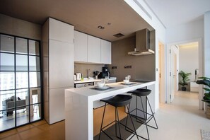 A modern kitchen with a central island, bar stools, and a view through a glass door. - 1B Walk to Metro, Marina Mall with Skyline Views (Dubai)
