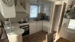 Een kleine keuken met witte kasten, een fornuis, oven en een spoelbak.