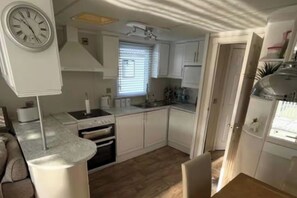 A compact kitchen with white cabinets, a stove, oven, and a sink. - Southview Holiday Park 2-bed Caravan, Sleeps 6 (Skegness)