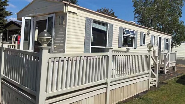 Een stacaravan met een omheind terras, een schotelantenne en een zichtbare garagedeur.