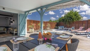 Een buitenruimte met eettafels voor twee personen, omringd door loungestoelen en een overdekte zithoek.