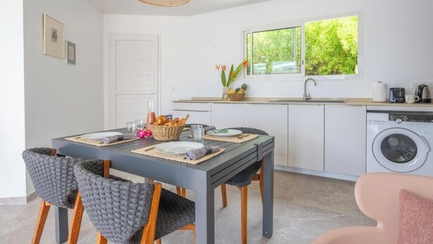 Een moderne keuken met een eethoek, een wasmachine en een raam met uitzicht op groen.