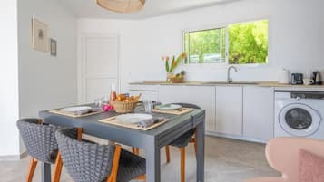 A modern kitchen with a dining area, a washing machine, and a window with a view of greenery.