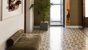 Un pasillo con piso estampado, una planta en maceta, un banco y una puerta que da a otra habitación.