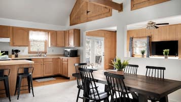 Une cuisine moderne avec des meubles en bois, un coin repas doté d’une grande table et de chaises, et un ventilateur de plafond.