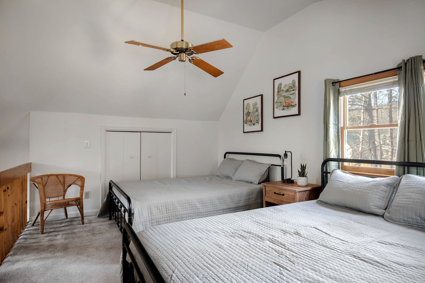 Une chambre avec deux lits, un ventilateur de plafond, une fenêtre avec des rideaux et une porte.