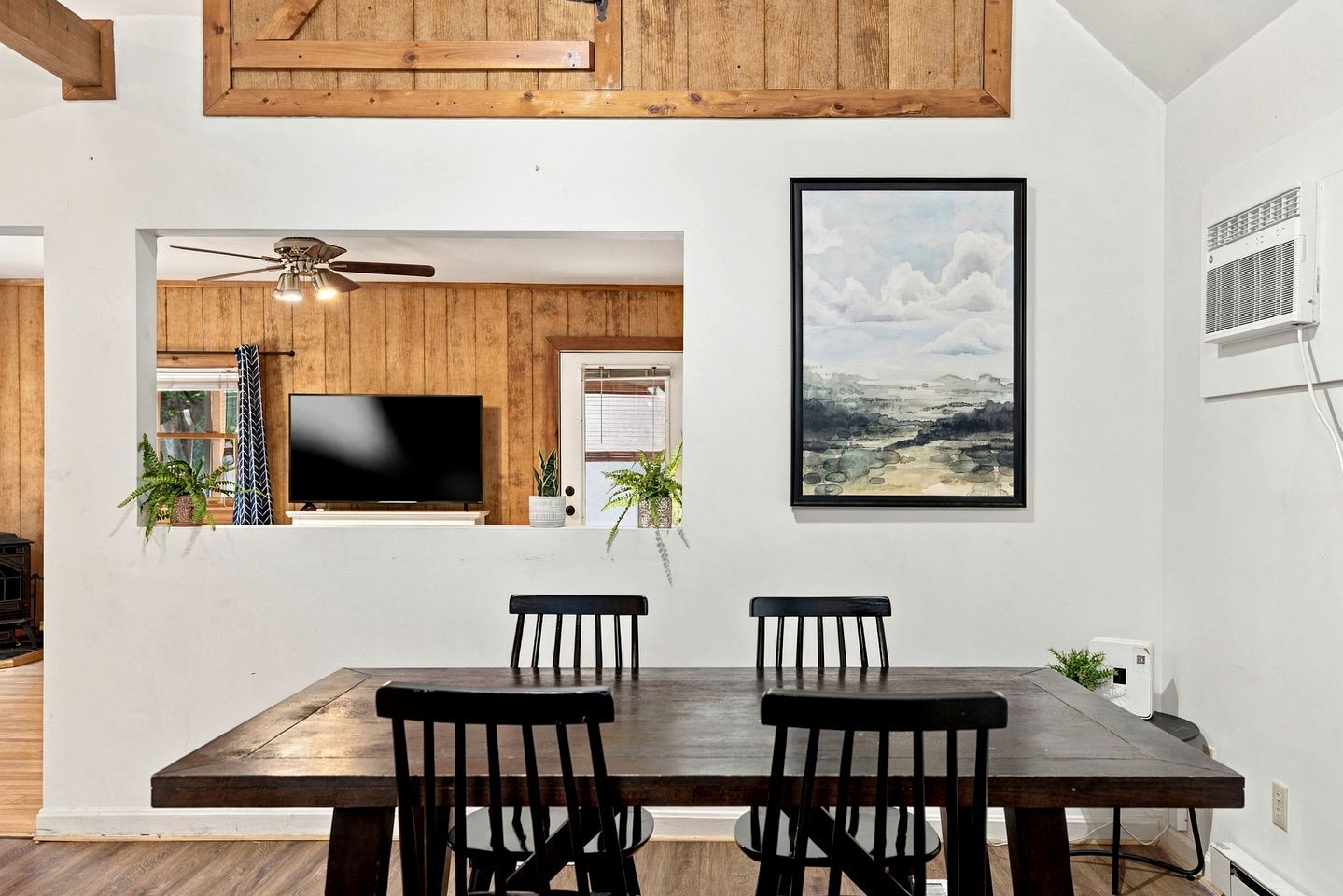 Un coin repas avec une table et des chaises en bois, un ventilateur de plafond et un tableau accroché au mur.