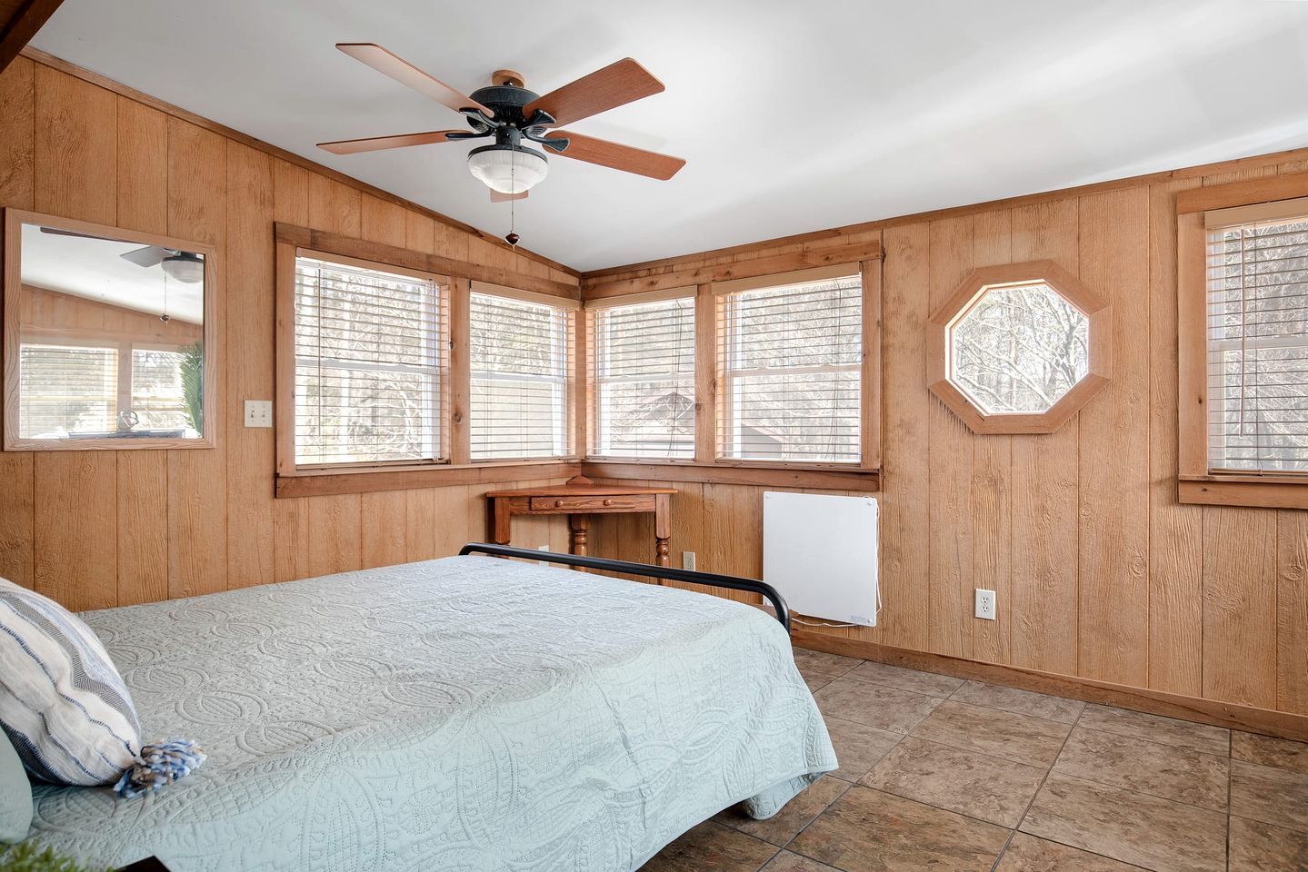 Une chambre à coucher avec un lit, un ventilateur de plafond, des murs en bois et de grandes fenêtres.