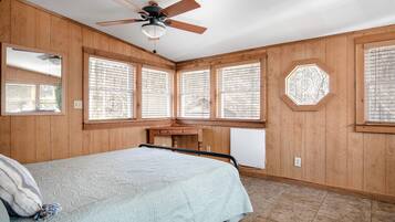 Une chambre à coucher avec un lit, un ventilateur de plafond, des murs en bois et de grandes fenêtres.