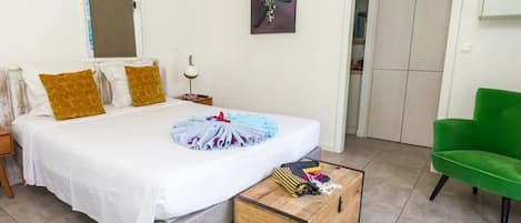 Un dormitorio con una cama, una silla verde, un cofre de madera y un cuadro en la pared.