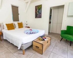 A bedroom with a bed, a green chair, a wooden chest, and a painting on the wall. - Jambiani Lodge - Mon'Désir Lodge | Martinique (Case-Pilote)