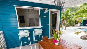 Una mesa de madera con sillas y un florero en un patio con pared azul y puerta de acceso al interior.