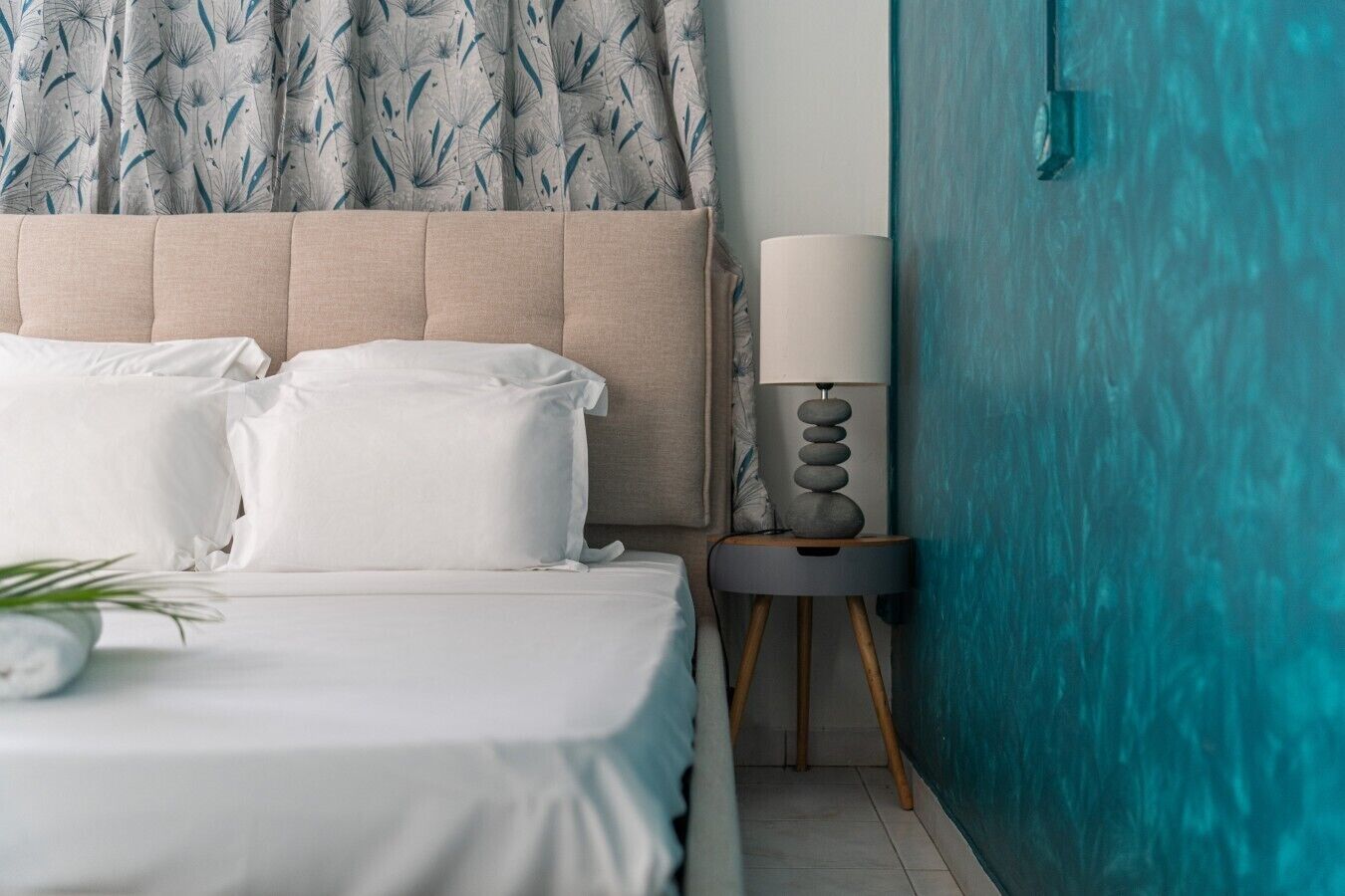 A neatly made bed with white linens, a bedside lamp, and a potted plant.