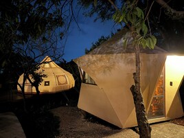 A tent-like structure with a door and windows, surrounded by trees and gravel.