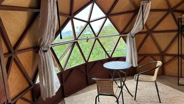 A cozy interior with a wooden dome ceiling, a round table, two chairs, and a view of greenery outside. - Gaiatri Holistic Glamping (Tepoztlán)
