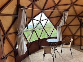 A cozy interior with a wooden dome ceiling, a round table, two chairs, and a view of greenery outside.