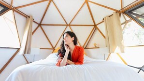 A person sitting on a bed inside a tent-like structure with a geometric wooden framework. - Gaiatri Holistic Glamping (Tepoztlán)