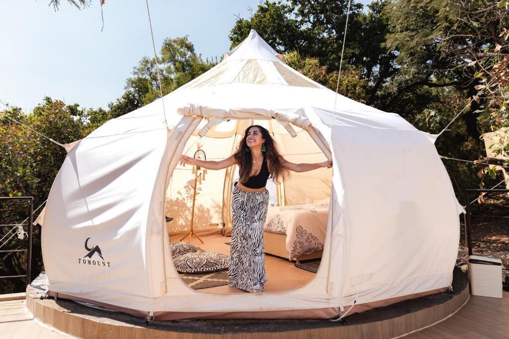Tienda de campaña con cama en su interior, rodeada de árboles.