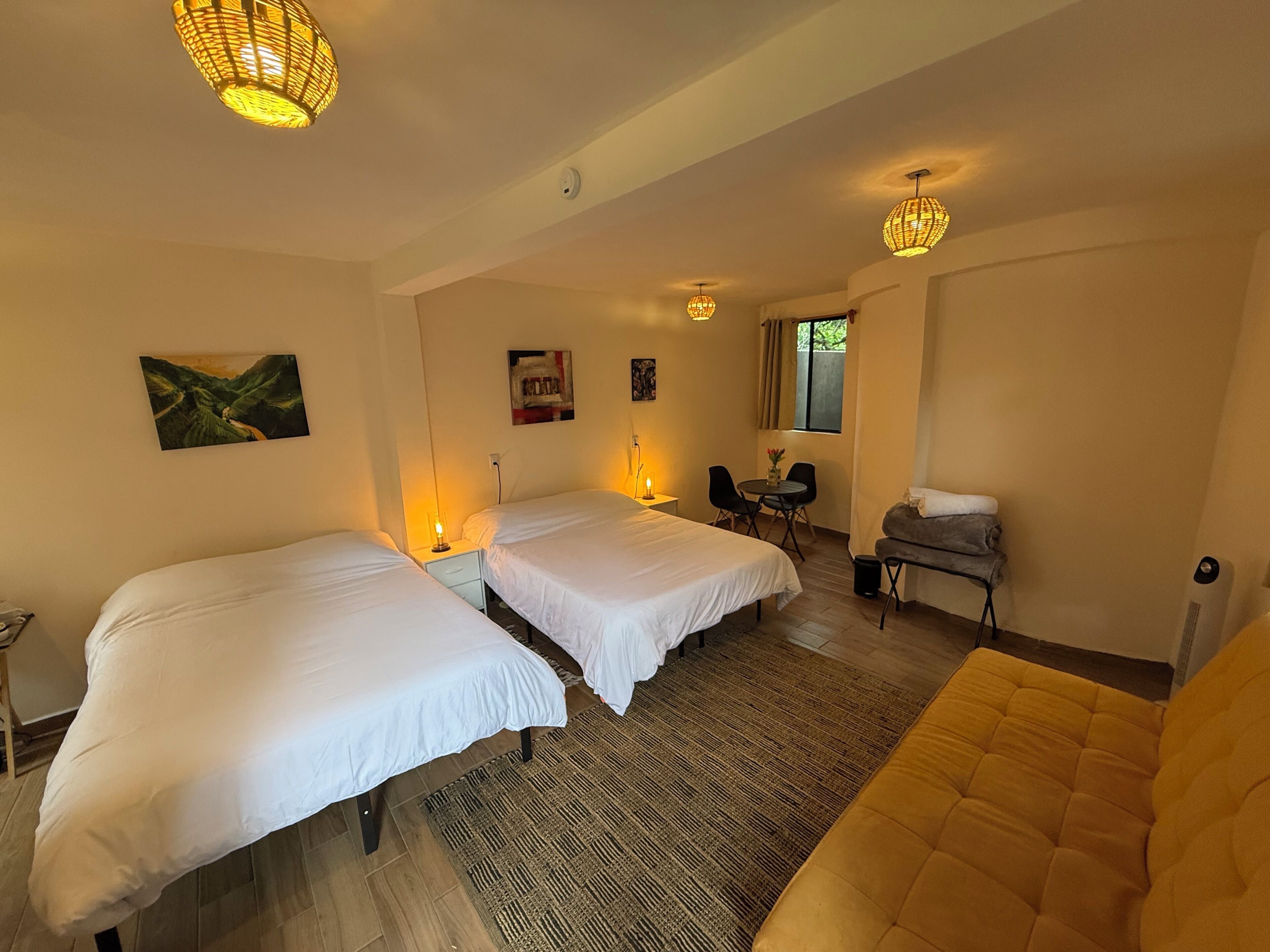 Habitación de hotel con dos camas, un sofá, una pequeña mesa con sillas y una ventana con cortinas.