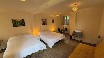 Habitación de hotel con dos camas, un sofá, una pequeña mesa con sillas y una ventana con cortinas.