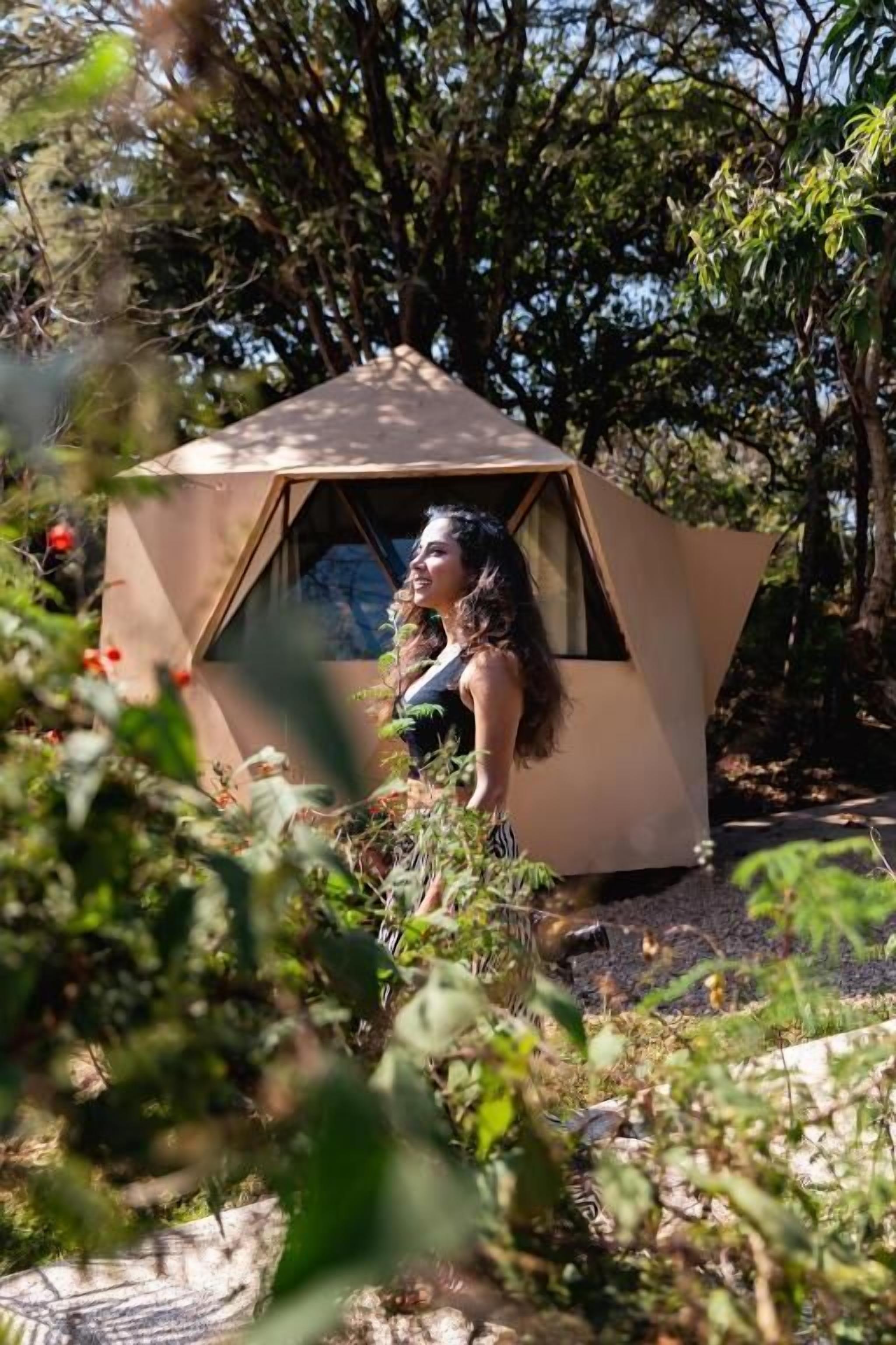 A geodesic dome structure with a person standing inside, surrounded by natural vegetation.