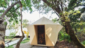 A small, single-room structure with a door, surrounded by trees and a gravel path. - Gaiatri Holistic Glamping (Tepoztlán)