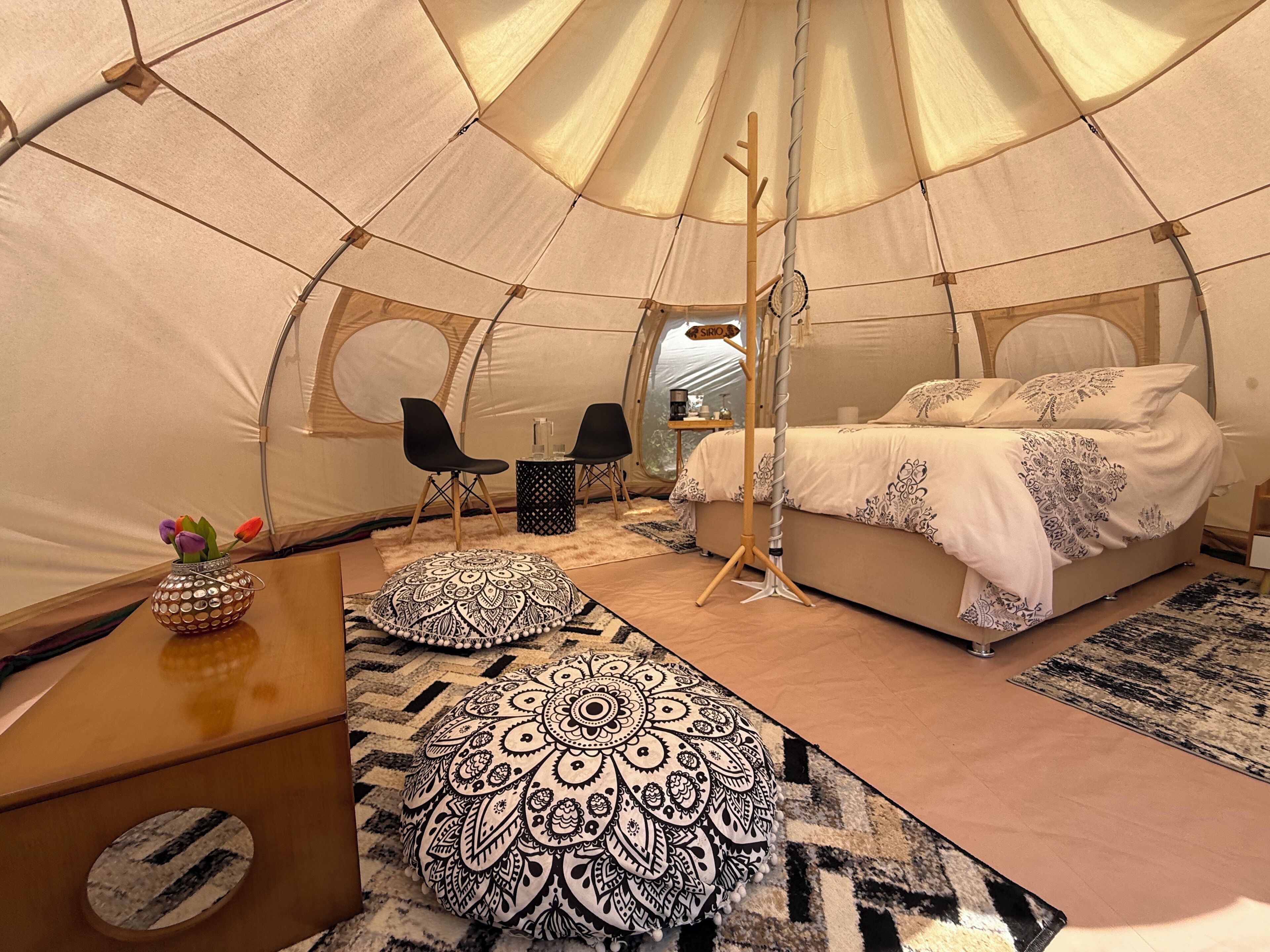 A cozy interior of a tent with a bed, two chairs, a small table, and decorative pillows.