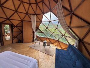 Una habitación con un ventanal grande, una cama, una silla y una mesita.