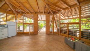 A spacious room with wooden beams, a kitchen area, and large windows allowing natural light. - Domaine De L'Anse Noire, right on the water (Les Anses-d`Arlet)