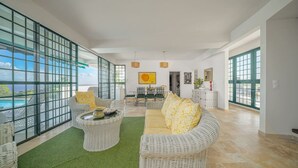 A spacious living area with a view of the ocean, wicker furniture, and a dining area with a table and chairs. - Villa Lala, a chic getaway with a pool and ocean view (Case-Pilote)