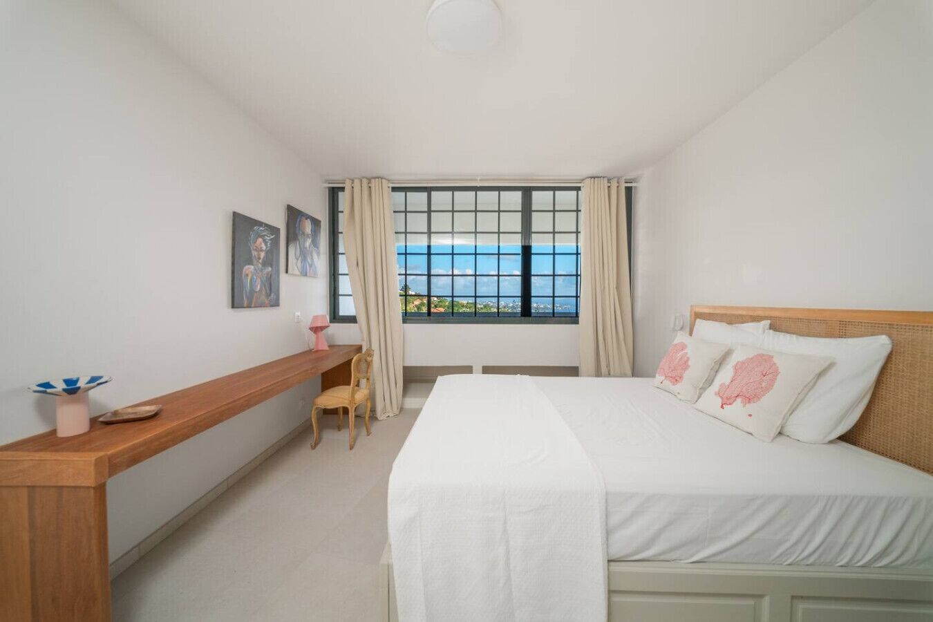 Une chambre à coucher comprenant un lit, un bureau, une chaise, une fenêtre avec des rideaux et des œuvres d’art accrochées au mur.