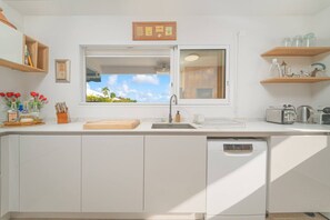 Una cuina moderna amb finestra, armaris blancs i vista a vegetació.